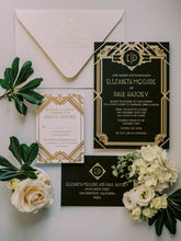 Load image into Gallery viewer, Photo of deco invitation suite from above. Black invitation with gold foil, black reply envelope with gold foil, white reply card with deco design in gold foil. White flowers and green leaves laying next to the invitation.