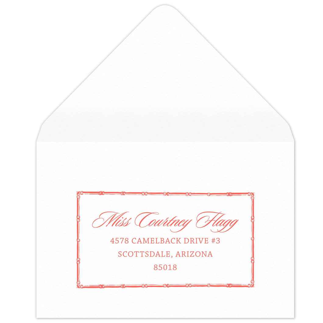 Bamboo rectangle holding block and script coral return address on a white envelope.